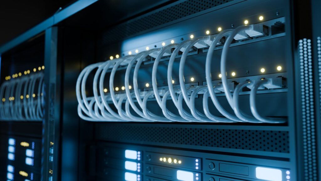 サーバーラックに整然と接続された白いLANケーブルと、青く光るネットワーク機器（サーバー環境のイメージ）